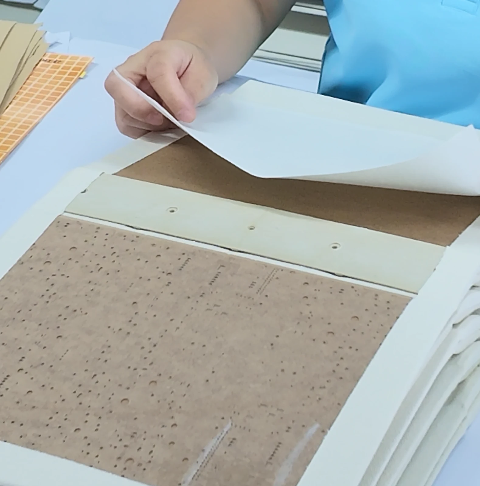 Paper lining being positioned over a board component by hand.
