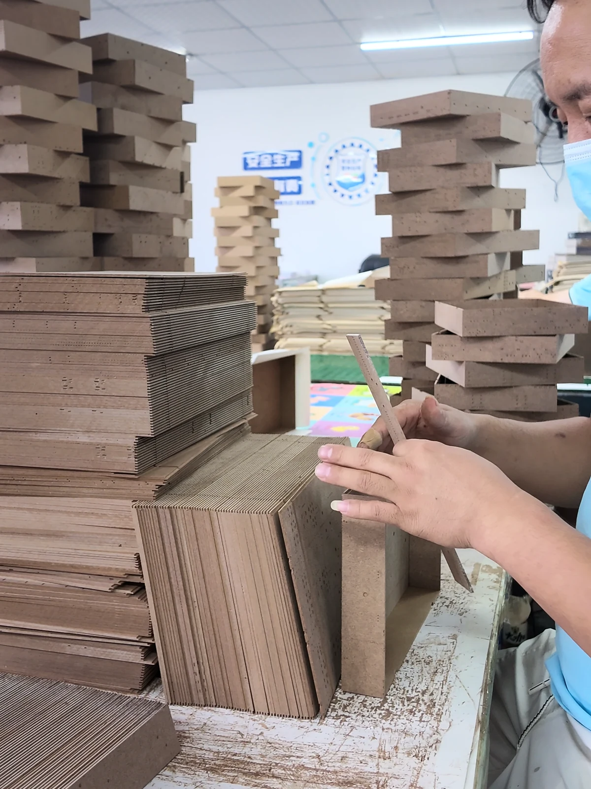 Stacks of unfinished rigid box shells and board components at an assembly station.