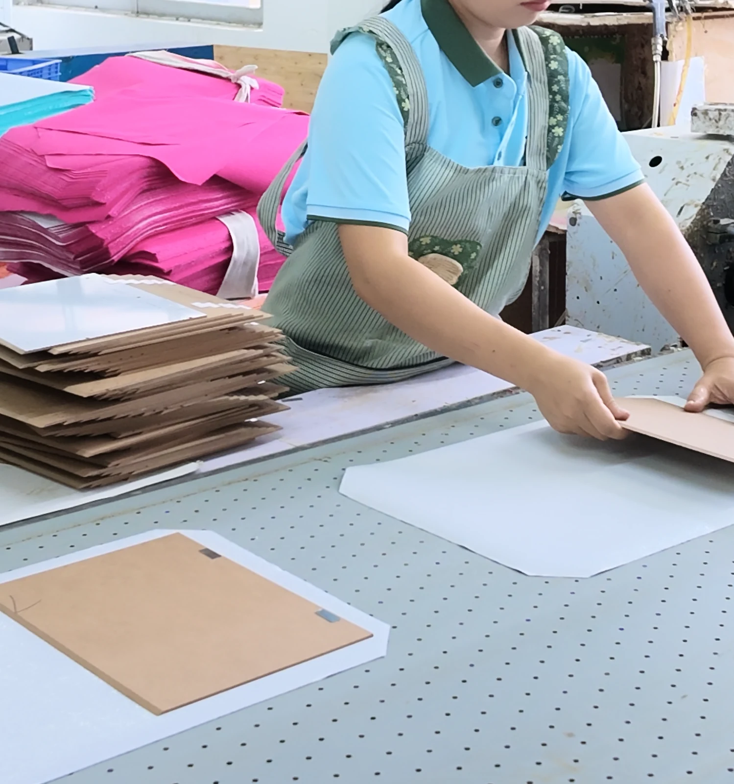 Paper and board aligned by hand on a perforated worktable.