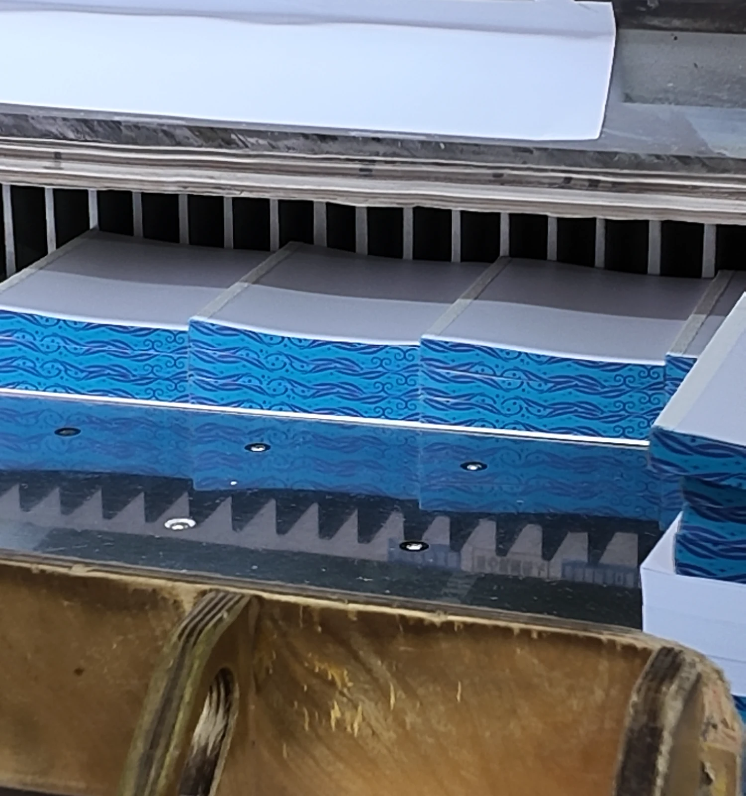 Paper stacks aligned under the guard of a cutting machine.