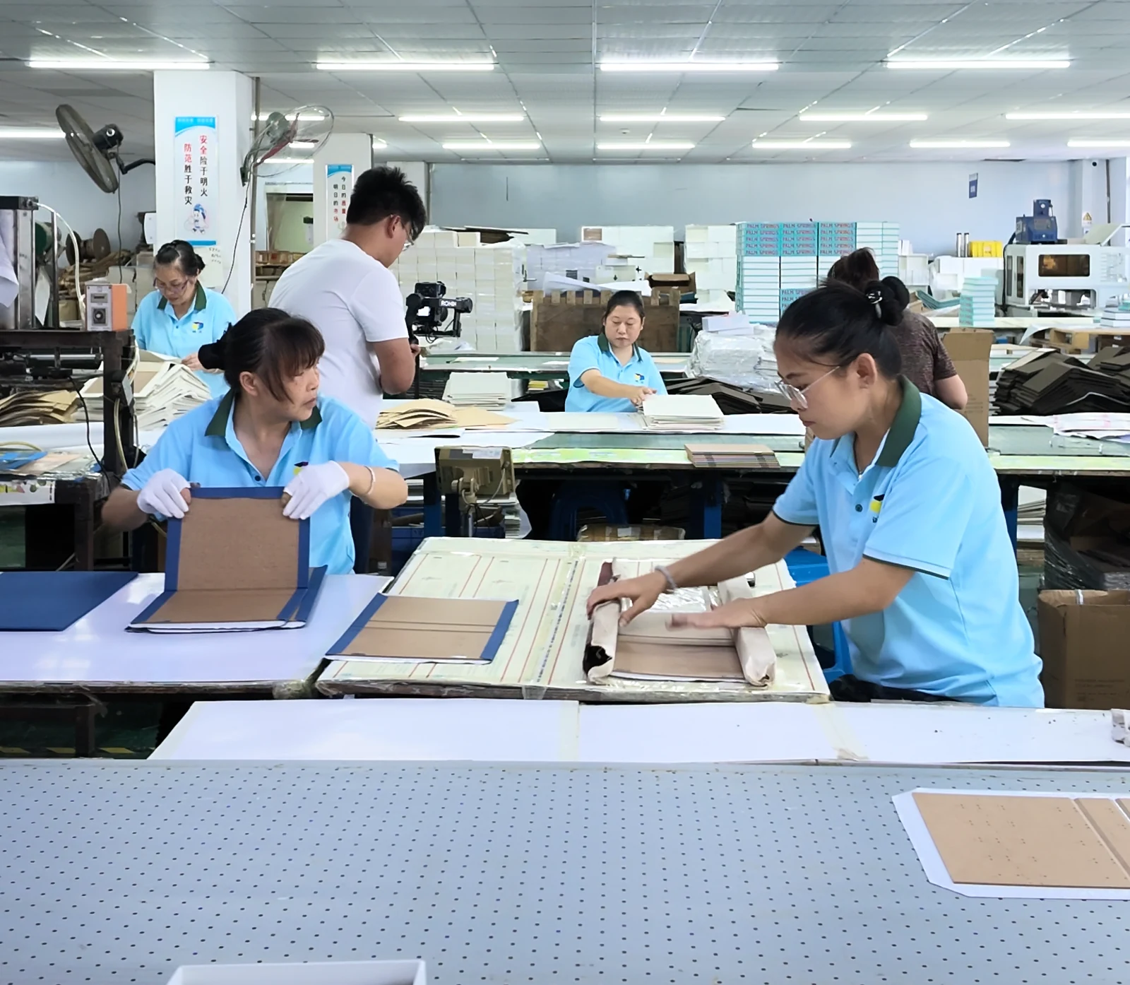 Workshop tables with operators assembling paper and board components.