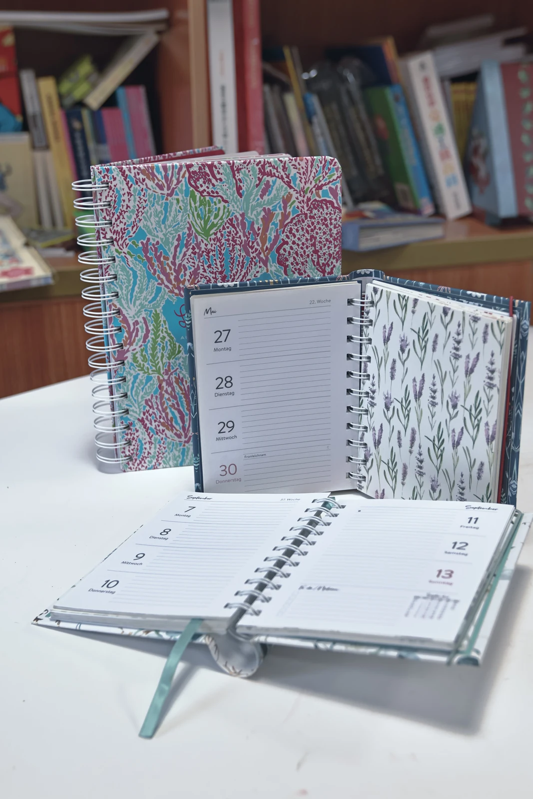 Wire-bound planners showing printed weekly pages, covers and a ribbon marker.